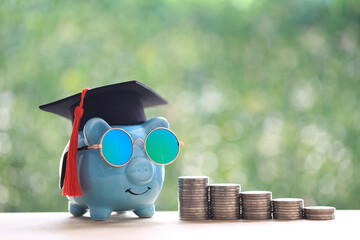 Graduation hat on piggy bank with stack of coins money on natural green background, Saving money...