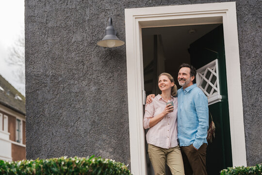 Smiling mature couple day dreaming at doorway of house