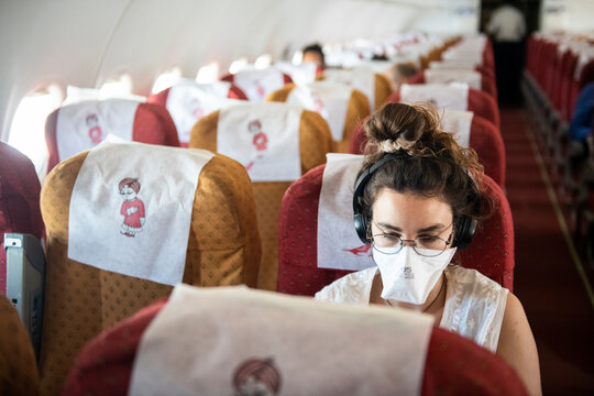 Young woman wearing a face mask while she listens to music on an almost empty plane, consequence of the Coronavirus pandemic of 2020.