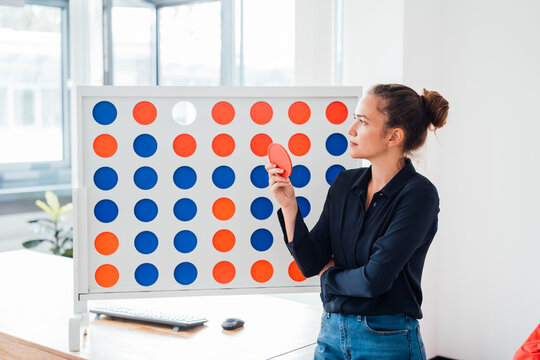 Thoughtful businesswoman standing by connect four game rack in office