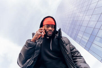 bottom view of healthy african american hip hop style young man looking at camera while talking on cell phone
