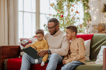 Father with daughter and son reading book on sofa at Christimas