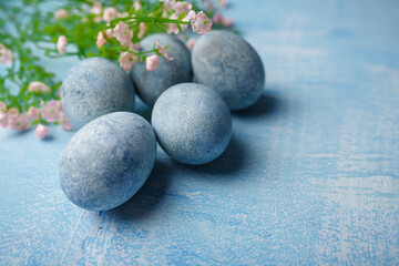 Painted Easter eggs on blue background with pink flowers. Spring holiday, symbolic food. Close up shot, copy space.