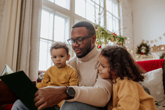 Man with daughters reading book on sofa at Christmas