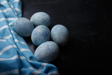 Easter eggs painted blue in white bowl on black wooden background with striped fabric. Close up shot, copy space