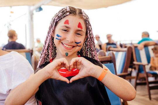 Smiling girl with face paint gesturing heart shape on yacht