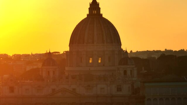 Tramonto sulla cupola di San Pietro a Roma.
Vista aerea, primopiano controluce della Basilica illuminata dal sole giallo
