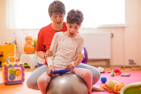 Physical therapist and girl with disability sitting on fitness ball in rehabilitation centre
