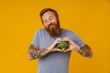 Bearded man holding broccoli while standing isolated over background