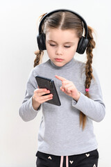 A girl with headphones and a phone on a white background, a girl with pigtails listens to music in headphones, photo with copy space.