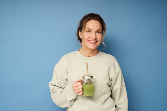 Happy woman standing with green smoothie against blue background