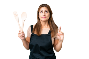 Middle age caucasian woman holding a rolling pin over isolated background with fingers crossing and wishing the best