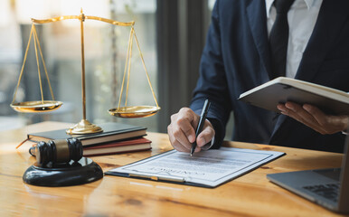 A young Asian lawyer or legal advisor opens a notebook and reads legal books and compares detailed information. Correct rules on sheet on file at an office desk.