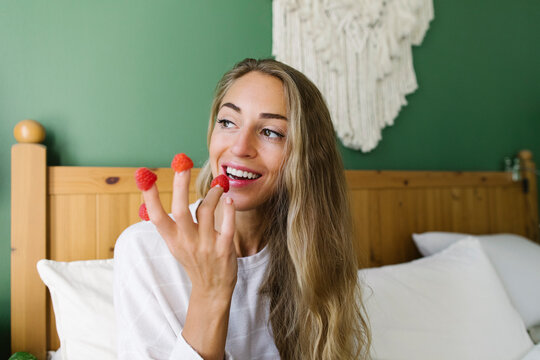 Happy Woman Eating Raspberries From Fingers At Home