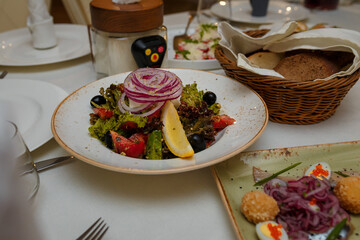 Festive table with appetizers. Greek salad with fresh vegetables, lemon and olives. Herring with onions, quail eggs with red caviar, cheese balls