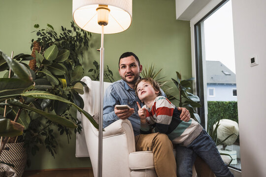 Son with father controlling light of floor lamp through smart phone