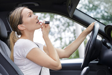 Fototapeta na wymiar female driver applying lipstick in visor mirror