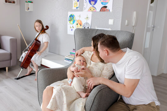 Parents holding baby boy with girl playing musical instrument in background