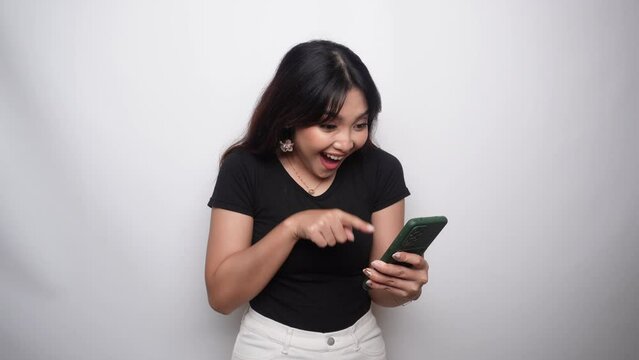 A portrait of a happy Asian woman dressed in black shirt and holding her phone, isolated by white background