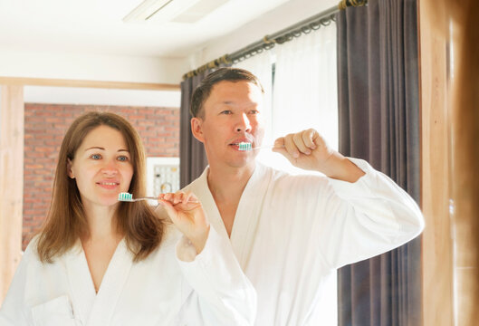 Asian man and woman in white bathrobe brushing teeth, oral care concept.