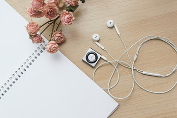 Top view of a wooden table on which lies an open notebook for notes on the rings dry roses and a small old player with headphones, vintage style copy space, mockup.