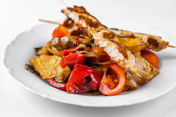 Souvlaki, pork meat on skewer on grilled juicy vegetable on white plate.