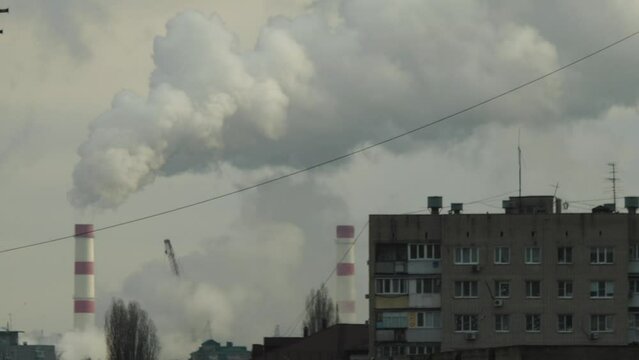Chimney of TPP with a column of smoke and a building of a high-rise apartment building. On the background of gray-yellow clouds. The global energy crisis. Urban landscape. Atmospheric pollution
