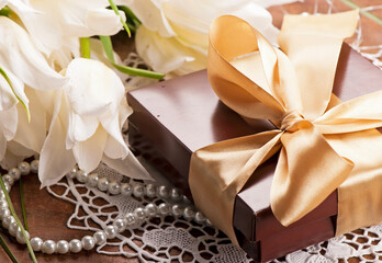 gift with a golden ribbon, and a bouquet of white tulips with green leaves. photo can be used as a postcard