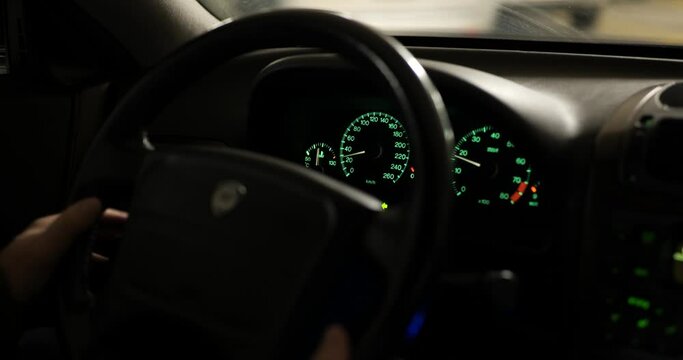 Analog car odometers or speedometer driving in dimly lit underground parking lot. Close up shot, green light, real time, unrecognizable male arms, metric values