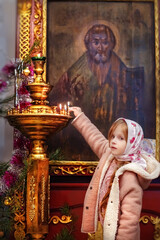 A little beautiful girl puts candles in the temple in the church. Orthodox holiday. Christian holiday. Prayer. Icons