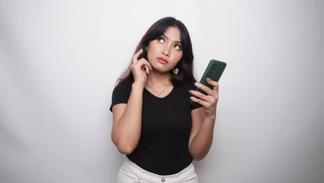 A thoughtful young woman in black shirt and holding her chin with phone on hand isolated by white background