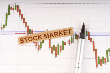 On the chart of business quotes lies a pen and torn paper with the inscription - STOCK MARKET