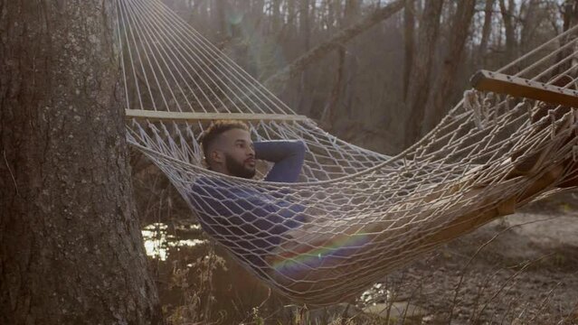 Dolly shot of thoughtful man relaxing on hammock in forest
