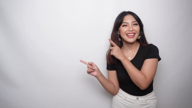 Excited Asian woman dressed in black shirt, pointing at the copy space beside her, isolated by white background