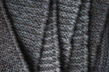 Dark gray knitted fabric folded in a zigzag pattern. Knitted texture background.