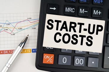 On the business chart lies a pen, a calculator and a business card with the inscription - start-up...