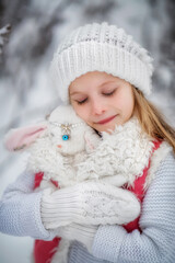 Beautiful little girl with long hair. Little girl in the winter forest. girl in a white knitted scarf. Girl in a Zara sheepskin coat. The little girl looks up to the sky. The little girl smiles. Snow.