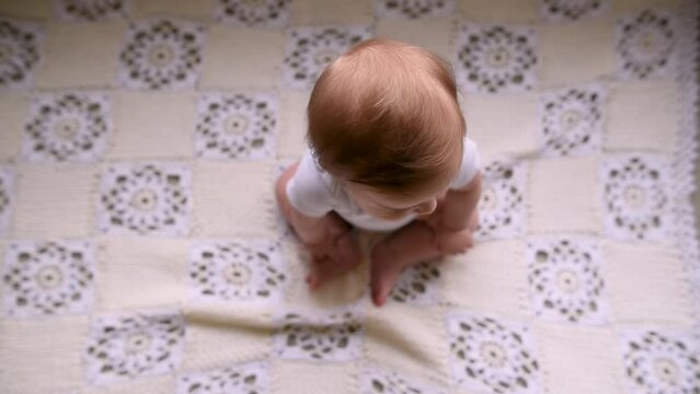 View from above of baby sitting on a crochet blanket on the floor