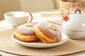 Breakfast table with Krapfen or berliner, or doughnut, or bombolone with cream filling. Tea cup and...