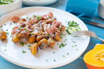 Pan fried pumpkin, potato gnocchi with ham, cheese and herbs on a plate. Gluten free dinner