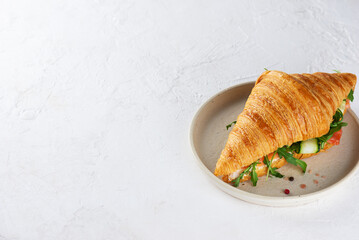 Croissant sandwich with salmon, cream cheese and arugula in a plate. Copy space.