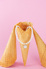 Pearl necklace or choker with a mother-of-pearl pendant in a waffle cone on a pink background,...