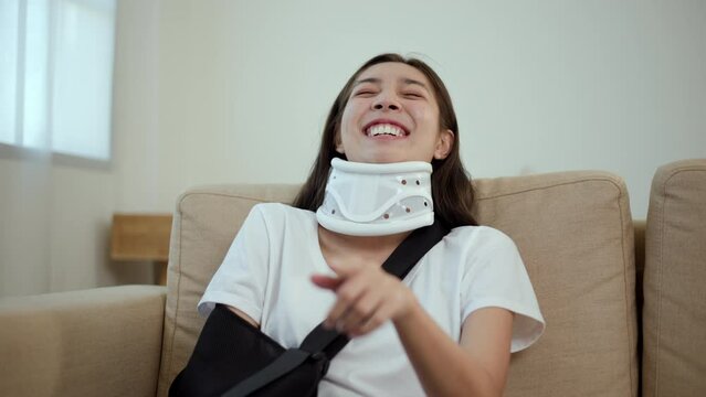Happy woman recovery watching tv using remote from accident fracture broken bone injury with leg splints in cast, neck splints collar, sling support arm. Social security and health insurance.