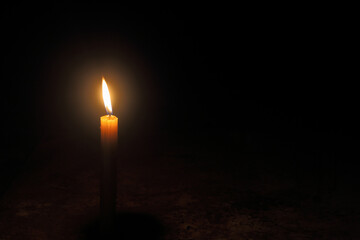 Light for a better life - Yellow candle on floor burns against the black background with copy space.