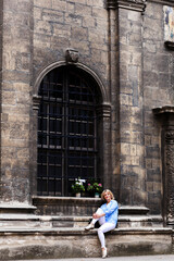Fototapeta na wymiar young blond woman sits against the background of a Gothic facade