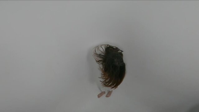 Cinematic footage of unrecognizable girl with face covered with  long red hair, dressed in straitjacket, barefoot, standing in a corner of white room. Ward in mental hospital. Horror psycho concept
