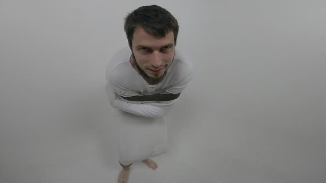 Portrait of a violent psychiatric patient. Young caucasian man in straitjacket with beard, dark hair and insane smile looking at the camera in white ward of asulym