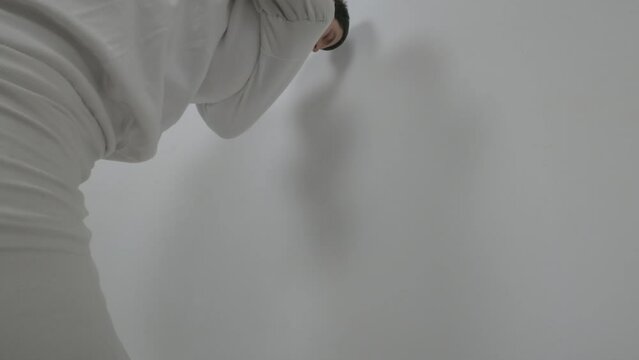 Portrait of a violent psychiatric patient. Young caucasian man in straitjacket with beard, dark hair and insane smile banging his head against wall  white ward of asulym