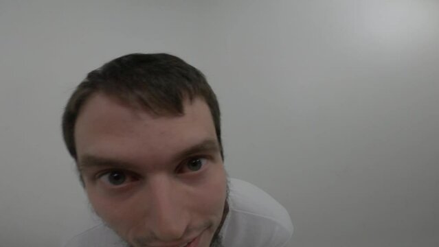 Portrait of psychiatric patient. Young caucasian man with insane smile moving in white room  trying to free from straitjacket in ward of asulym. Treatment of schizophrenia in psychiatric clinic