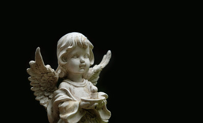 Statue of angel baby with candle on abstract blurred black background close up. concept of faith,...